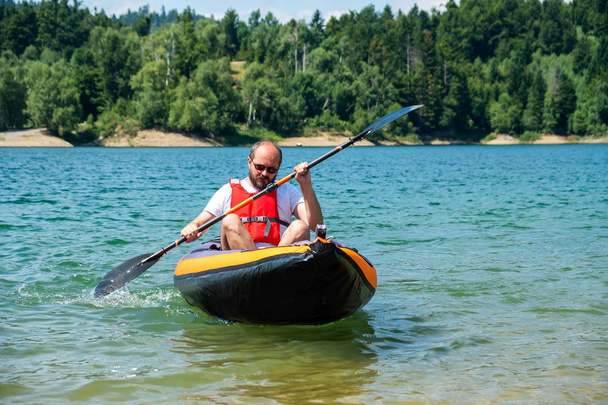 Mies melomassa puhallettavassa kajakissa järvellä Lokve, Gorski kotar, Kroatia. Jännitystä melonta kokemus kauniissa luonnossa
. - Valokuva, kuva