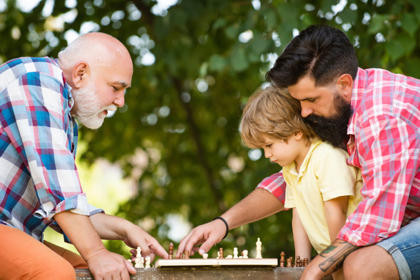 Family holiday and togetherness. Young boy with father and grandfather enjoying together in park. Male Multi Generation Family. Kid Playing Chess. - Fotó, kép