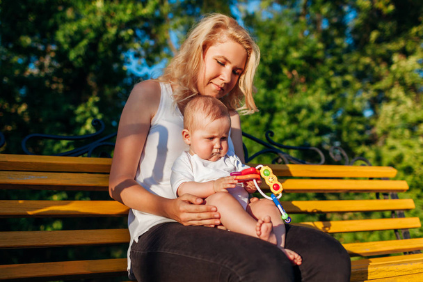 Baby girl playing with toys sitting on her mom's knees in summer park. Family having fun outdoors - Foto, Bild
