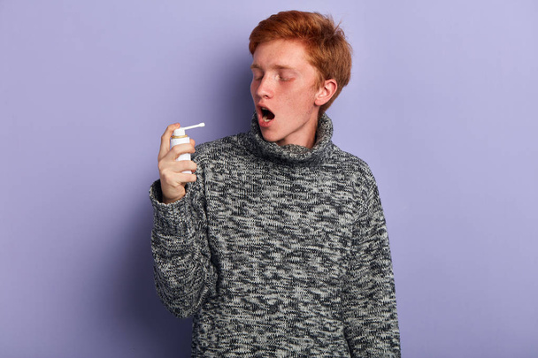 sick man with wide open mouth sprays a medicine - Foto, afbeelding
