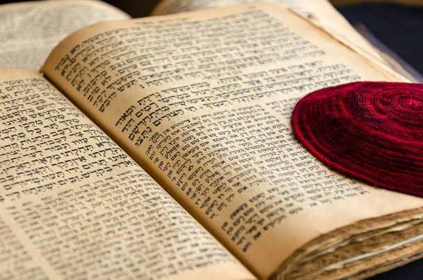Otwarta stara księga żydowska. Czerwona dzianina żydowska beli leży na otwartej stronie Pisma Świętego. Selektywne skupienie. Zbliżenie tekstu hebrajskiego - Zdjęcie, obraz