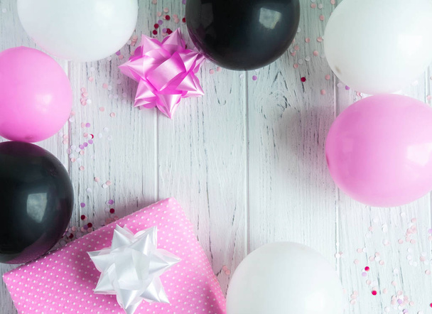 Design frame for birthday card background. Pink, white and black balloons with a gift box on a light wooden background. Greeting card design - 写真・画像