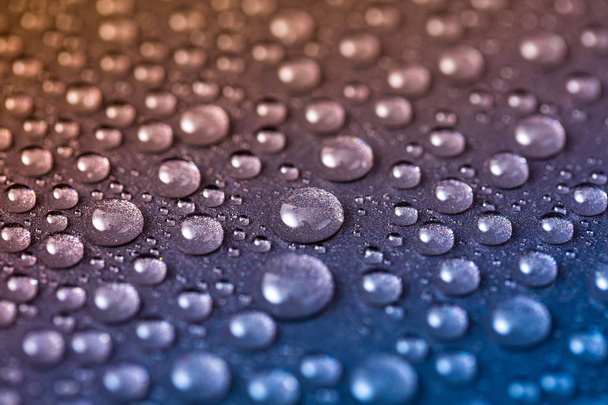 Wassertropfen auf glänzender und körniger Metalloberfläche, abstrakter blauer und gelber Hintergrund mit nassen Tropfen - Foto, Bild