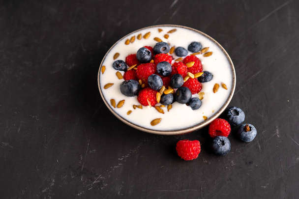 Tasty fresh blueberry raspberries  yoghurt shake dessert in ceramic bowl standing on black dark table background.  - Foto, Imagem