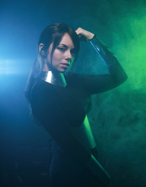 futuristisches Mode-Model trägt schwarze und silberne Kleidung und steht im farbenfrohen blauen und grünen Rauch - Foto, Bild