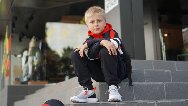 Niño en traje de entrenamiento posando con baloncesto en frente de la tienda
. - Foto, imagen