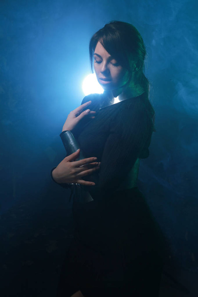 футуристическая модель в черно-серебристой одежде, стоящая в ярком синем и зеленом дыму
 - Фото, изображение