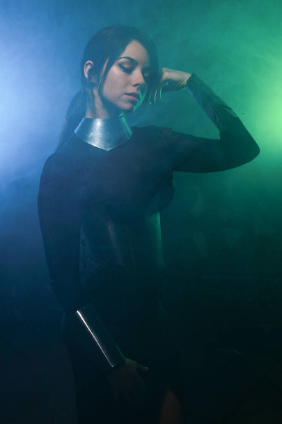 futurystyczny model mody ubrany w czarne i srebrne ubrania i stoi w kolorowym niebieskim i zielonym dymem - Zdjęcie, obraz