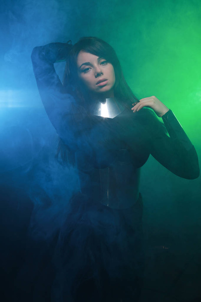 futurisztikus divatmodell visel, fekete és ezüst ruhát, és állva a színes kék és zöld füst - Fotó, kép