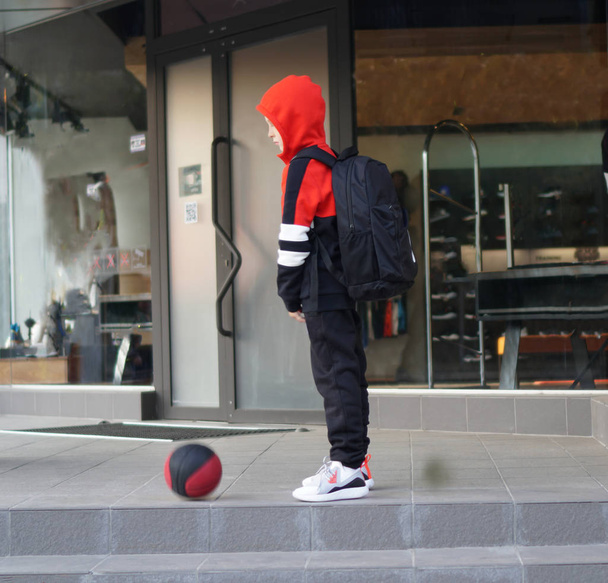 Młody chłopak w garniturze treningowej stwarzających z koszykówkę przed sklepem. - Zdjęcie, obraz