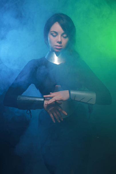 modèle de mode futuriste portant des vêtements noirs et argentés et debout dans la fumée bleue et verte colorée
 - Photo, image