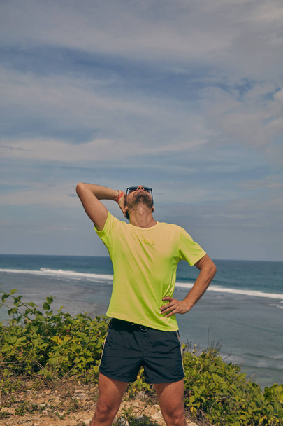 Sportsman stretching on a tropical exotic cliff near the ocean. - Φωτογραφία, εικόνα