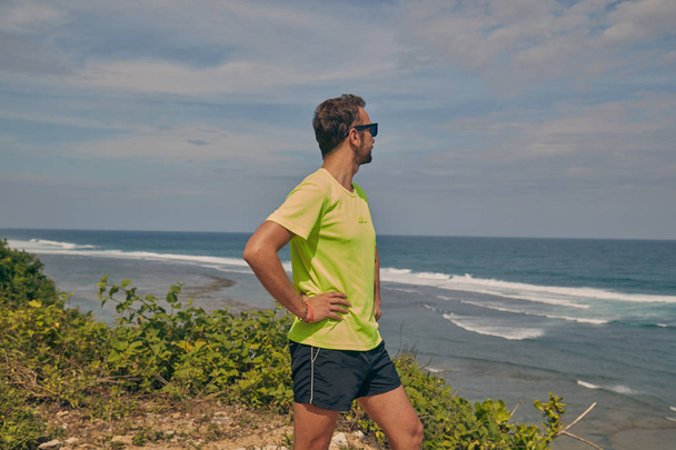 Sportsman stretching on a tropical exotic cliff near the ocean. - Photo, Image