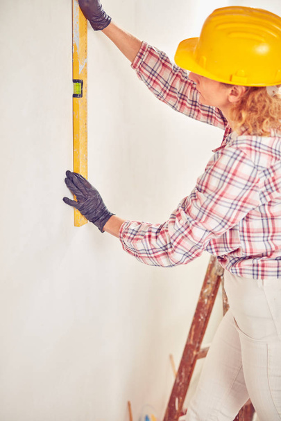 Mujer trabajadora enyesando / pintando paredes dentro de la casa
. - Foto, Imagen