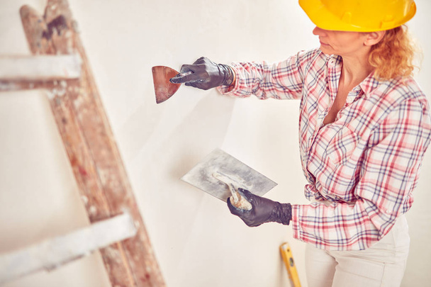 Working woman plastering / painting walls inside the house. - Photo, Image