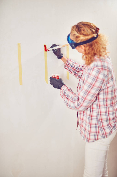 Robocza kobieta tynkowanie/malowanie ścian wewnątrz domu. - Zdjęcie, obraz