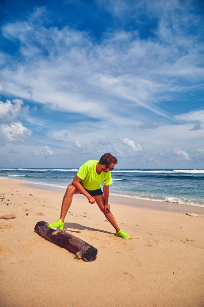 Deportista estirándose en una playa de arena tropical
. - Foto, Imagen