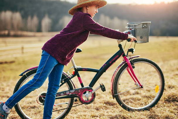 Schattige kleine tien jaar oud meisje paardrijden fiets op het platteland. - Foto, afbeelding