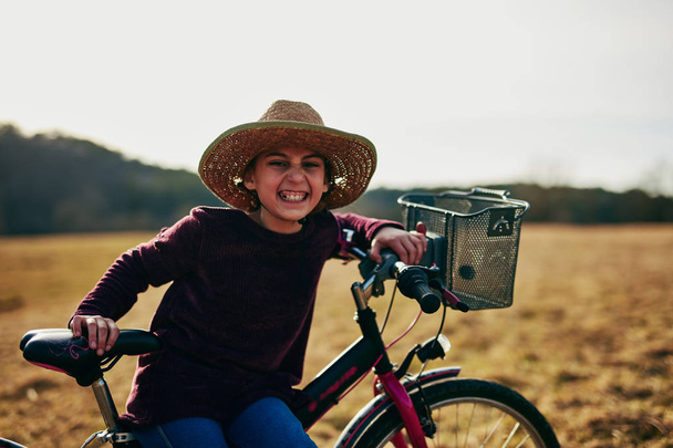 Roztomilá holčička, desetiletá dívka jezdila na kole na venkově. - Fotografie, Obrázek