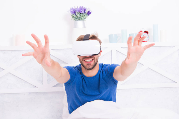 Using computer technology to create a simulated environment. Happy guy wearing VR headset for computer gaming. Handsome man playing virtual computer games in bed. Gaming computer - Fotografie, Obrázek