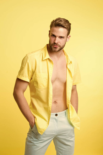 Want to see sexy torso. It is hot here. I will show you my sexy body. Man handsome bearded guy undressing yellow background. Guy confident attractive macho feels sexy while unbuttoning shirt - Fotó, kép