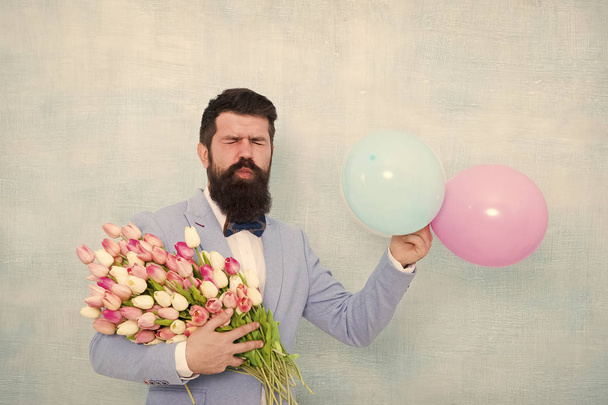 Gentleman making romantic surprise for her. Flowers delivery. Gentleman romantic date. Birthday greetings. For someone special. Man bearded gentleman suit bow tie hold air balloons and bouquet - Фото, изображение