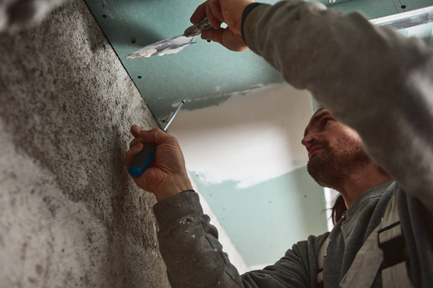 Работник оштукатурирует гипсовые стены внутри дома
. - Фото, изображение