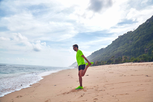 Спортсмен тягнеться на тропічному піщаному пляжі
. - Фото, зображення