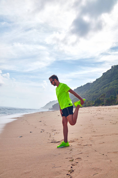 Sportsman rozciągający się na tropikalnej piaszczystej plaży. - Zdjęcie, obraz