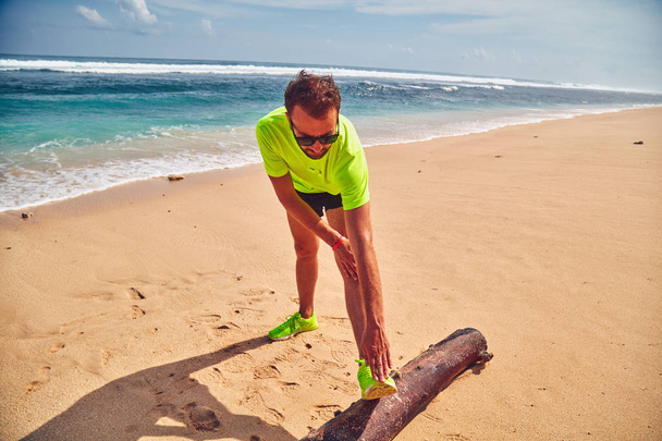 Deportista estirándose en una playa de arena tropical
. - Foto, imagen