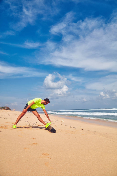 Αθλητικός αθλητής που απλώνεται σε τροπική αμμώδη παραλία. - Φωτογραφία, εικόνα