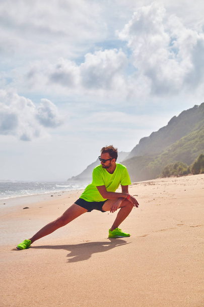 Sportsman stretching on a tropical sandy beach. - Zdjęcie, obraz