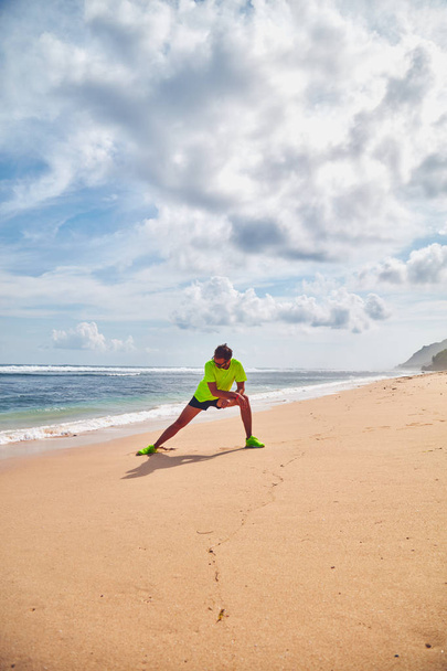 Sportsman stretching on a tropical sandy beach. - Zdjęcie, obraz
