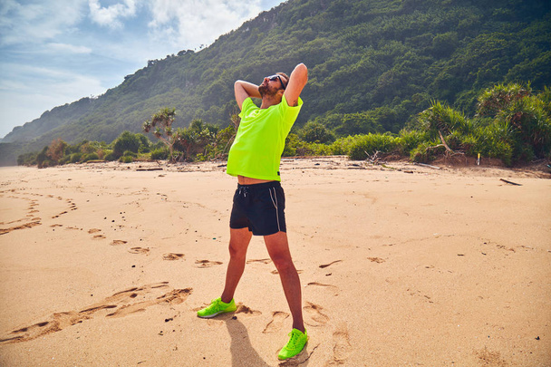 Esportista que se estende em uma praia tropical de areia
. - Foto, Imagem