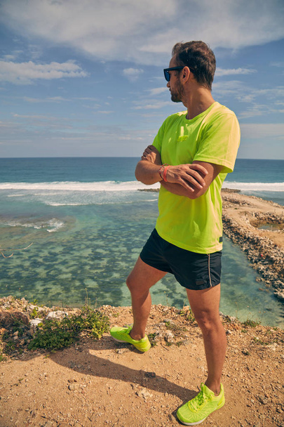 Sportsman stretching on a tropical exotic cliff near the ocean. - Zdjęcie, obraz