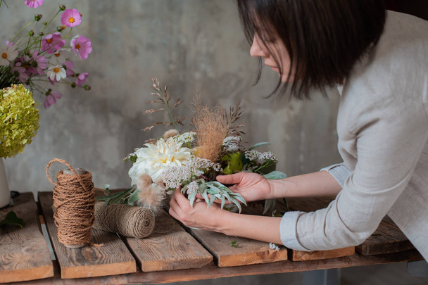 Female professional florist prepares the arrangement of wild flowers. - Фото, зображення