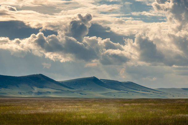 Трави пагорбів на горизонті в степу під важкі хмари небо під час заходу з сонячними променями сонця в Хакасії, Сибіру, Росія. - Фото, зображення