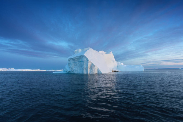 Valokuvauksellinen ja monimutkainen jäävuori alla mielenkiintoinen ja sininen taivas auringonlaskun aikana. Ilmaston lämpenemisen vaikutus luontoon. Käsitteellinen kuva sulavasta jäätiköstä syvänsinisessä vedessä Etelämantereella tai Grönlannissa
 - Valokuva, kuva