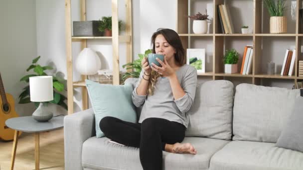 Young girl drinks coffee from a large cup in a cozy living room - Felvétel, videó