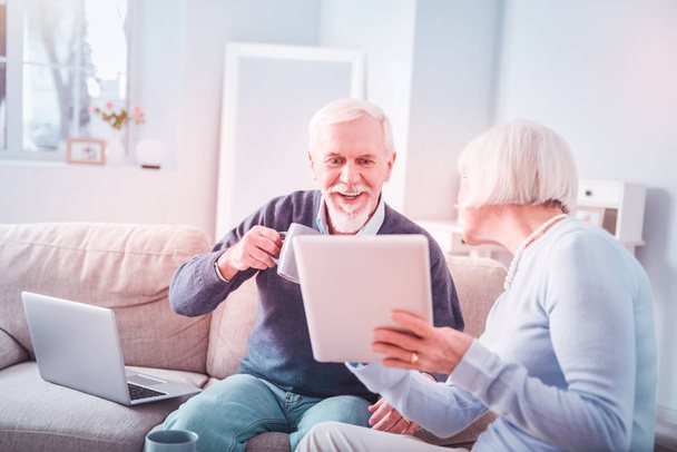 Modern retired woman holding her tablet showing husband some photos - Zdjęcie, obraz