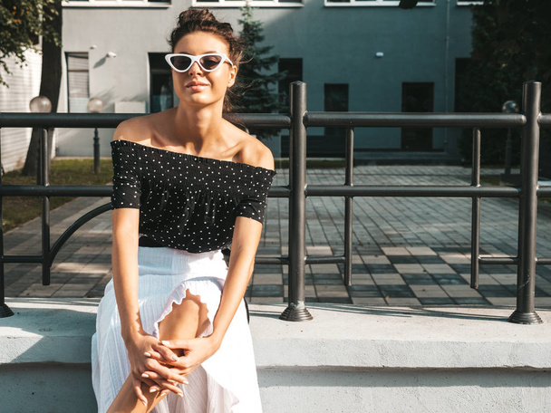 Beautiful smiling model dressed in elegant summer clothes.Sexy carefree girl sitting in the street background.Trendy modern businesswoman in sunglasses having fun - Фото, зображення