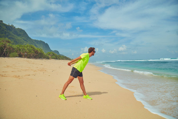 Αθλητικός αθλητής που απλώνεται σε τροπική αμμώδη παραλία. - Φωτογραφία, εικόνα