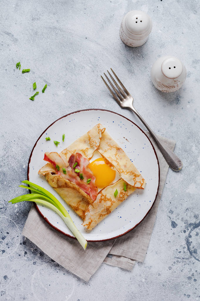 Krepy z jajkiem sadzonym, ser, boczek i zielonej cebuli na śniadanie na jasnoszarym tle betonowych. - Zdjęcie, obraz