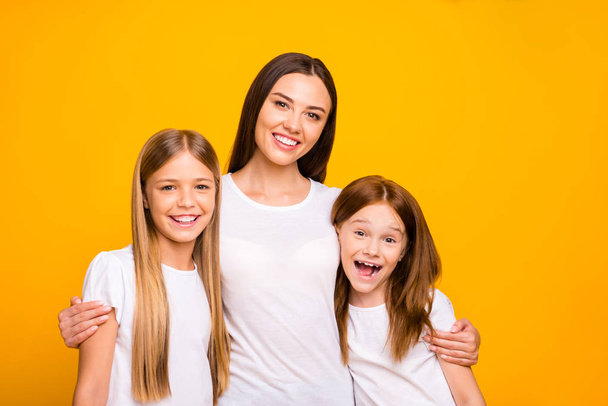 Two small ladies with young nanny hugging wear casual white t-shirts isolated yellow background - Фото, зображення