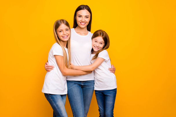 Two small ladies hugging young and beautiful babysitter wear casual white t-shirts isolated yellow background - Foto, immagini