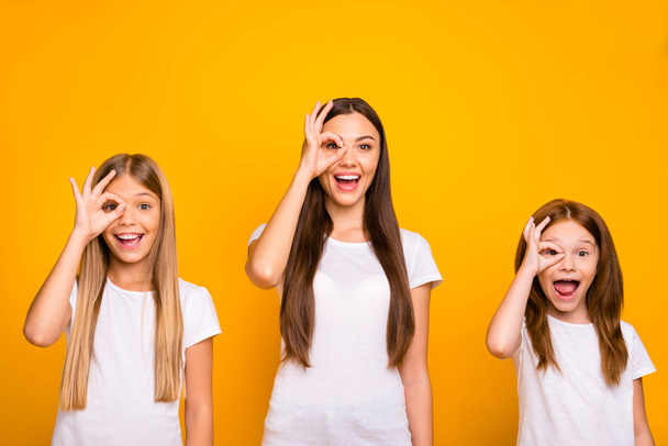 Funny three sister ladies holding hands in okey symbols near eye like specs wear casual outfit isolated yellow background - Foto, Imagen