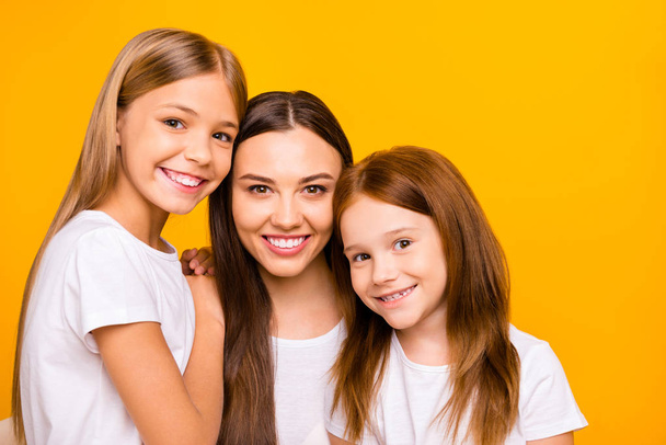 Three pretty ladies of different age hugging each other with love wear casual white t-shirts isolated yellow background - Foto, Imagem