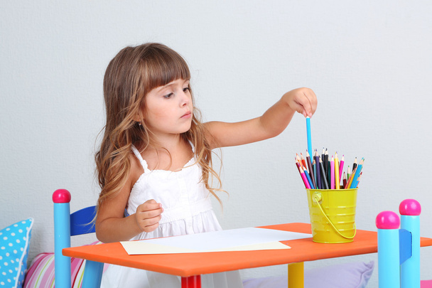 Little girl draws sitting at table in room on grey wall background - 写真・画像