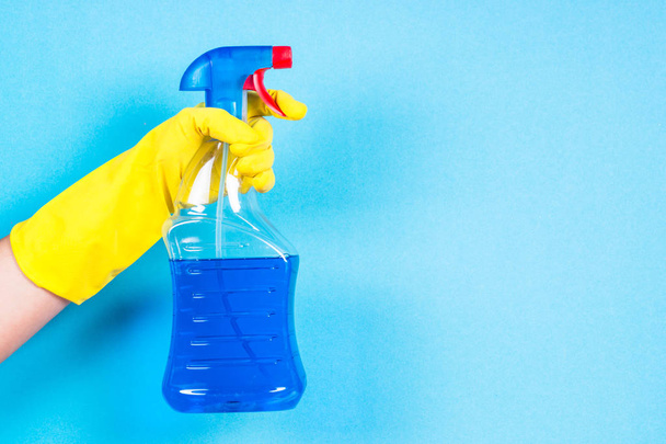 Рука в жовтих рукавичках тримає пляшку засобу для чищення на синьому фоні
. - Фото, зображення