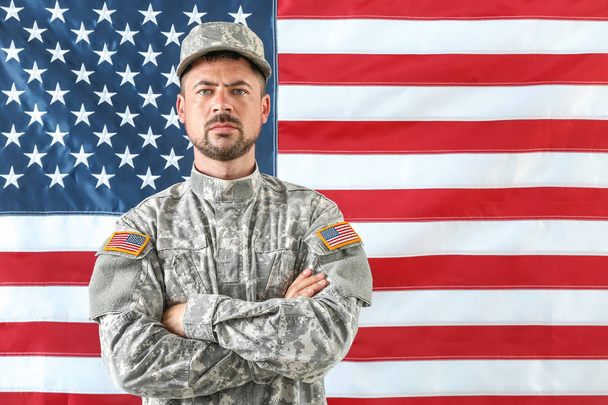 Soldado em camuflagem com bandeira nacional dos EUA em segundo plano
 - Foto, Imagem